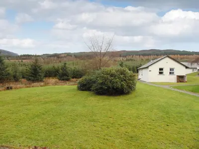 a house in the middle of a field with a bush at Pine Cottage in Killin