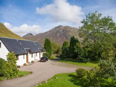 a house in the mountains with a car parked in the driveway at Aonach Cottage - Uk41932 in Glencoe