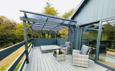 a deck with a pergola and chairs on a house at Riverview Lodge & Luxury Hot Tub in Acharra