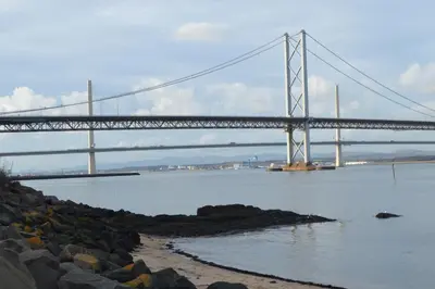 a bridge over a body of water with rocks in the foreground at Carnegie Holiday Cottage in Dunfermline