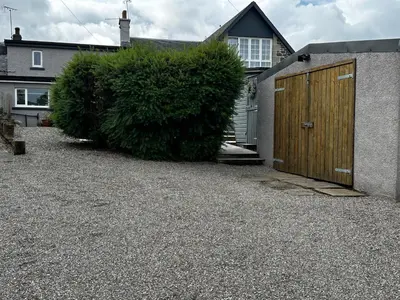 a house with a wooden door in a gravel driveway at Thornhill cottage with views of the Trossachs in Thornhill