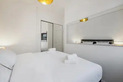 a white bedroom with a white bed and a mirror at George St Getaway in Ayr