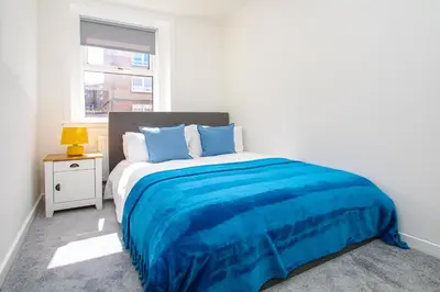 a bedroom with a bed with blue sheets and a window at Tobago Urban Apartment in Greenock