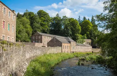 an old brick building with a river in front of it at New Lanark Self Catering Waterhouses in Lanark