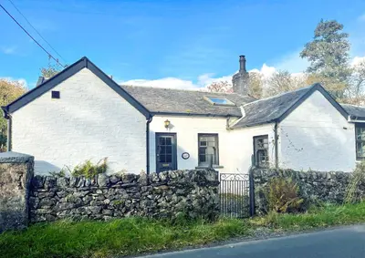 a white house with a stone wall at Old Powdermill Cottage in Tighnabruaich