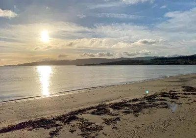 a beach with the sun reflecting on the water at Old Powdermill Cottage in Tighnabruaich