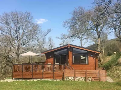 a log cabin with a deck and an umbrella at Teaghlach Luxury Lodge with hot tub Balquhidder Mhor Lodges in Lochearnhead