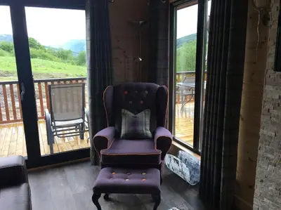 a living room with a chair and a balcony at Teaghlach Luxury Lodge with hot tub Balquhidder Mhor Lodges in Lochearnhead