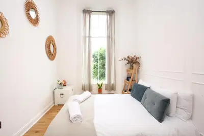 a white bedroom with a large bed in a room with a window at Lovely spacious 2 Bed Flat in Glasgow
