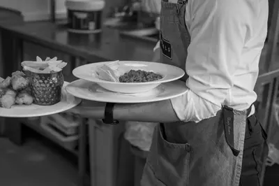 a chef holding a plate of food on a counter at Angels Hotel in Uddingston