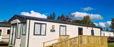 a small white tiny house with a wooden deck at Lochgilphead Caravan Park in Lochgilphead