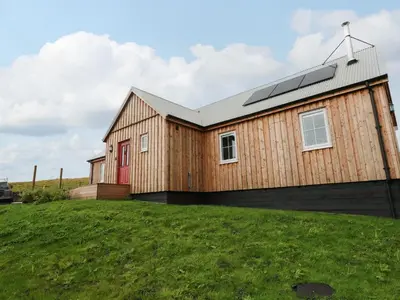 a wooden house with a red door on a grass field at Tirlaggan Úr in Oban