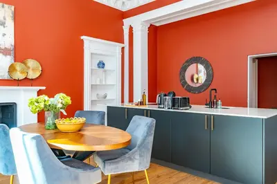 a kitchen with orange walls and a wooden table and chairs at Dragon Suites Luxury Apartments at 9 Albyn Place in Edinburgh