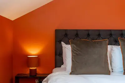 a bedroom with a bed with an orange wall at Dragon Suites Luxury Apartments at 9 Albyn Place in Edinburgh