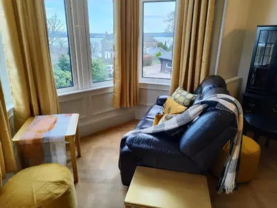 a living room with a leather couch and windows at Bella Vista Manor - with elevated views over Rothesay & Loch Striven in Rothesay