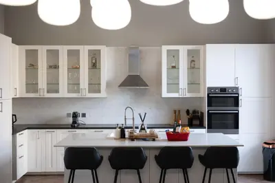a kitchen with white cabinets and a kitchen island with black chairs at Extravagant 6 Bed Victorian Townhouse with Hot Tub in Glasgow