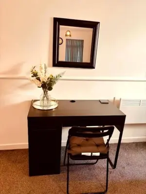 a desk with a vase of flowers and a mirror at Modern apartment in Stenhousemuir in Stenhousemuir