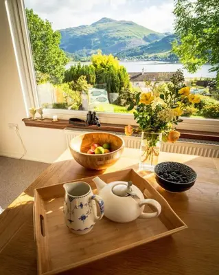 a tray with a tea kettle and a bowl of fruit on a table at Sachsblick in Lochgoilhead