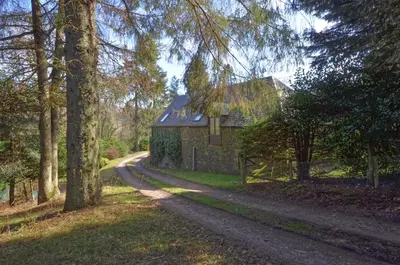 a dirt road next to a stone house with trees at Black Barony Home Farm Cottage in Eddleston