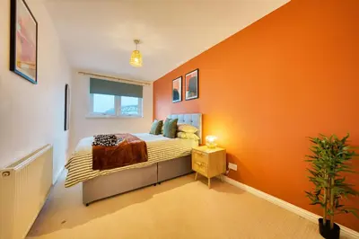 a bedroom with an orange wall with a bed at 2BR Flat Central Location with Free Parking in Glasgow