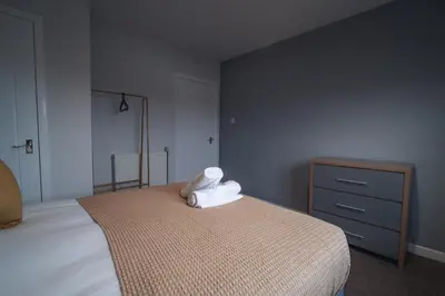 a bedroom with a bed with white sheets and a dresser at Franklin Place in East Kilbride