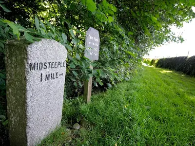 a stone sign in the grass next to a bush at Beautiful Cottage in Historical Robert Burns Farm - Pass the Keys in Dumfries