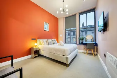 a bedroom with orange walls and a bed and a window at Grand Central Station 2 Bed Apartment A1 in Glasgow