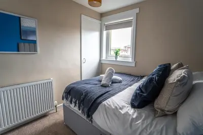 a bedroom with a bed with blue sheets and a window at Skye House in Grangemouth