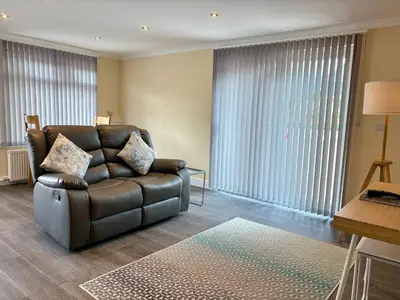 a living room with a leather couch and large windows at Barra Cottage in Ballachulish