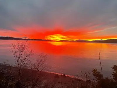 a sunset over a body of water with the sun setting at Tumpseys Hideaway with Hot Tub & Sunset Loch Views, Glencoe Near Fort William in Ballachulish