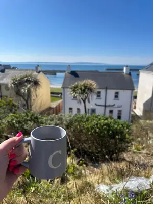 a person holding a cup of coffee on the beach at Church Bay House Rathlin in Rathlin Island