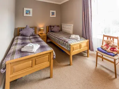a twin bedroom with two beds and a chair at Littlebay Apartment in Oban