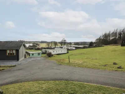 an empty road next to a field with houses at Debonair Lodge in Newton Stewart