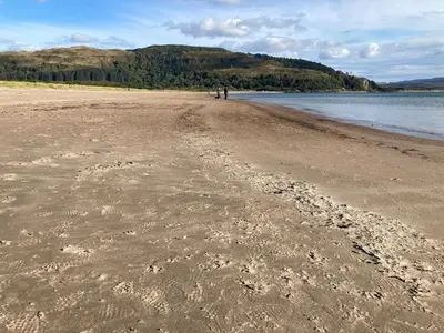 a beach with footprints in the sand and water at The Old Shed in Benderloch