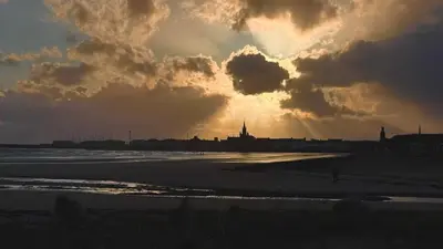 a sunset over a beach with a city in the background at West Coast Home From Home in Stevenston