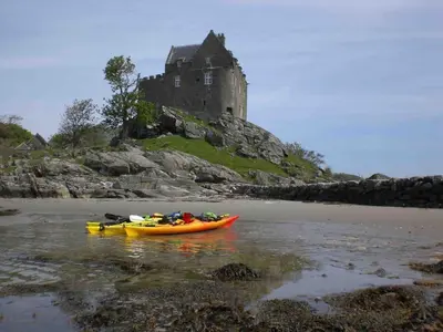 a kayak on the beach with a castle in the background at Cosy Karibu cottage with stunning canal views in Cairnbaan