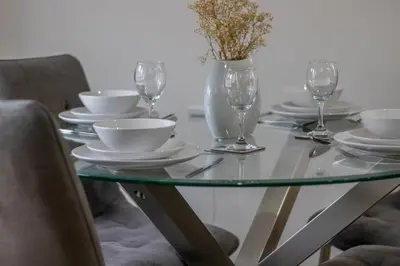 a glass table with plates and wine glasses on it at The Larky - Modern 2 Bed Cottage in Larkhall in Larkhall