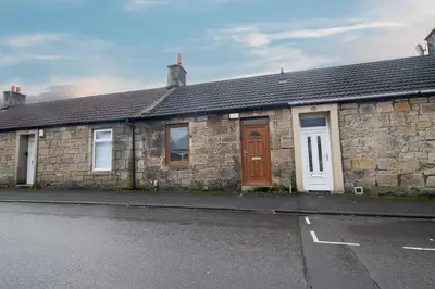 a stone house with brown doors and a street at The Larky - Modern 2 Bed Cottage in Larkhall in Larkhall