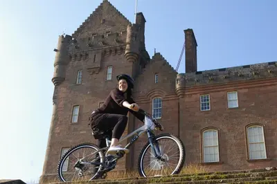 a woman riding a bike in front of a castle at The Shorehouse in Brodick
