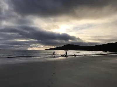 two people standing on a beach with the ocean at Cala Fearnadh Off-Grid cabin, Bunessan, Mull in Bunessan