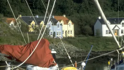 a house in the background with a boat in the water at Craobh Haven Cottages in Craobh Haven
