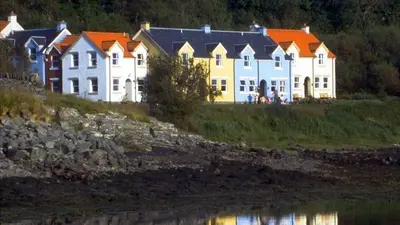 a row of houses on a hill next to a body of water at Craobh Haven Cottages in Craobh Haven
