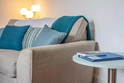 a couch with pillows and a table with a book at Number Two Aberdour - Pretty Village nr Edinburgh in Aberdour