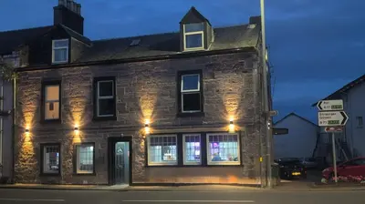 an old brick building with lights in the windows at The Cassillis Hotel - Smart Self Check-in Hotel & Bar in Maybole