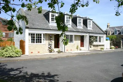 a white house with white windows on a street at Church Cottage with sunny garden in Ayr