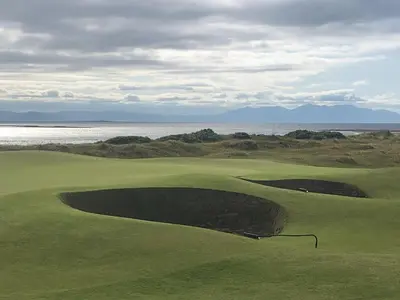 a view of a golf course with the ocean in the background at Church Cottage with sunny garden in Ayr