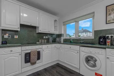 a white kitchen with white cabinets and a window at Vacant Nests The Grampian Free Wifi in Wishaw