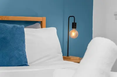 a bedroom with a bed with a blue wall and a lamp at Vacant Nests The Grampian Free Wifi in Wishaw