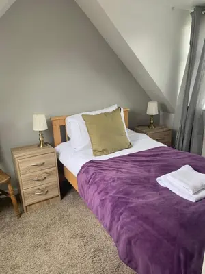 a bedroom with a large bed with a purple blanket at Campbell Cottage in Biggar