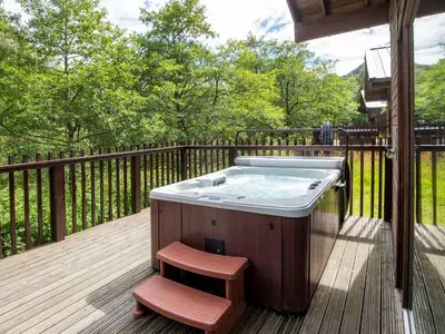 a hot tub sitting on a deck with a stool at Strathyre, Ben Ledi Cabins - Forest Holidays in Callander